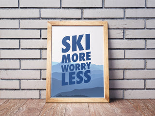 En tavla lutad mot en tegelstensvägg. Poster med grafiskt motiv och texten ski more worry less.